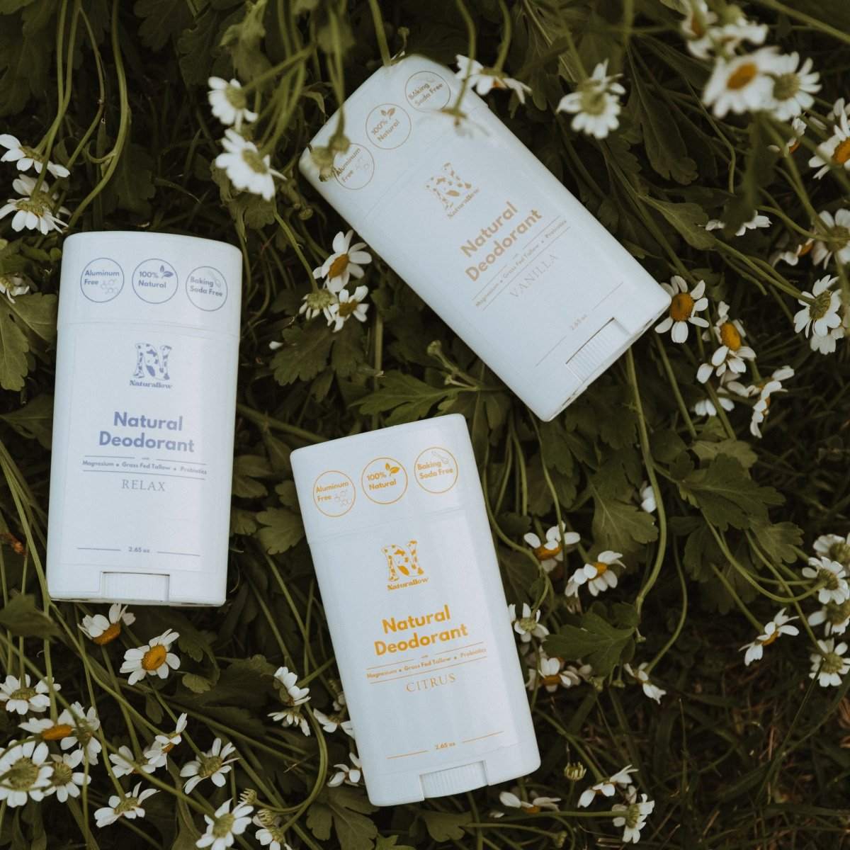 3 of Naturallow's Natural Deodorants, Citrus, Relax, and Vanilla, lying on a bed of greenery and flowers