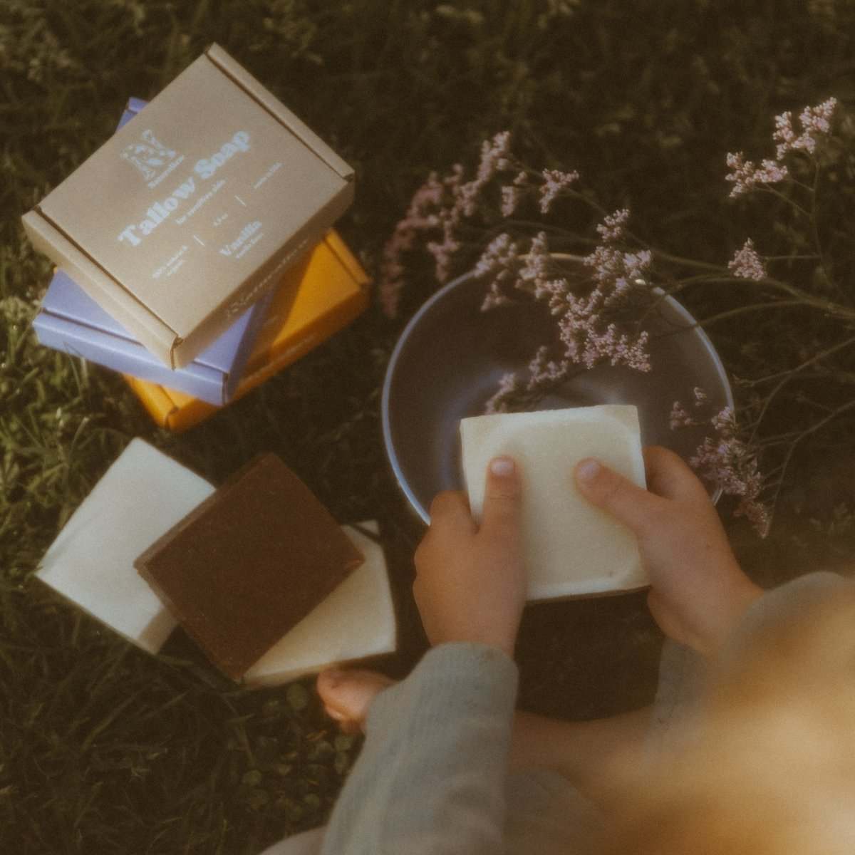 A 1st person POV Naturallow Tallow Soap Bar lathering in a small hands with other soap bars stacked next to them