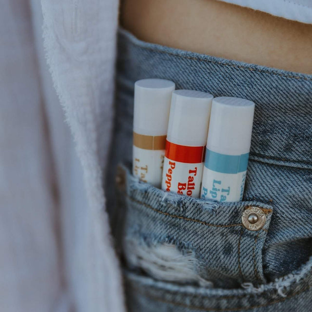 3 of Naturallow's Vanilla, Peppermint, and Pure Unscented Tallow Lip Balms Side-By-Side in a Persons Jean Pants Pockets