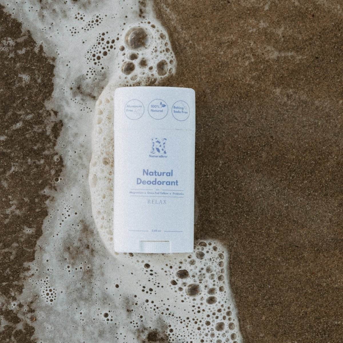 Naturallow's Relax Natural Deodorant lying on the sand in the shallow beach surf