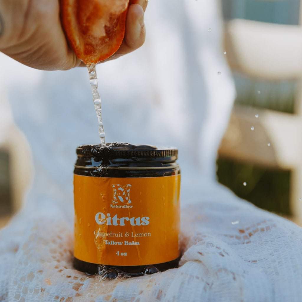 Naturallow's Citrus Tallow Body Balm Jar for dry skin on a white lace surface with citrus juice being squeezed onto it