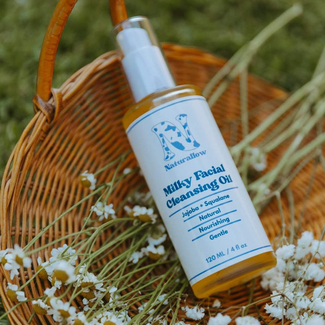 Naturallow's Milky Facial Cleansing Oil bottle sitting in a woven basket with flowers