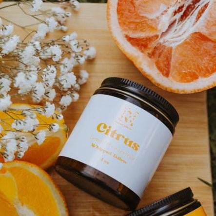 Naturallow's Citrus Whipped Tallow Moisturizer for dry skin on a cutting board next to flowers and slices of citrus fruits