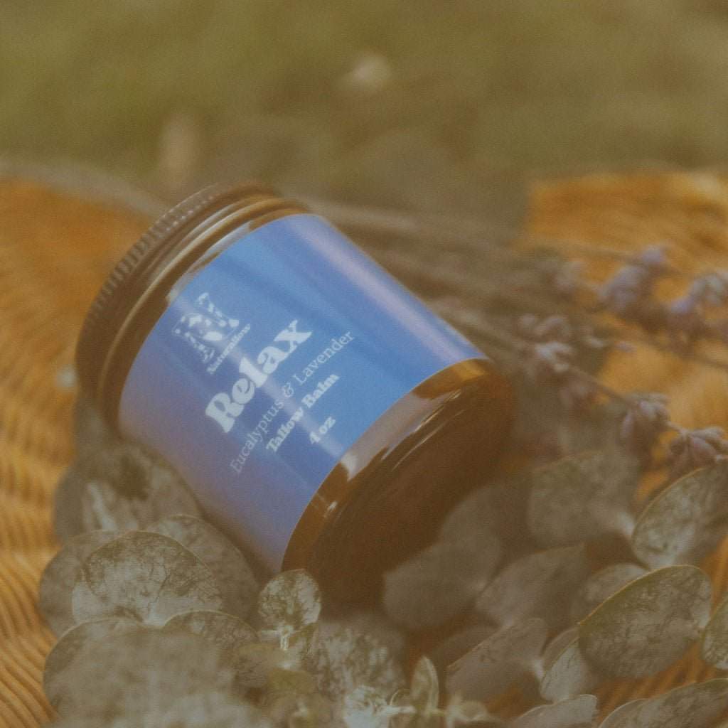 Naturallow's Relax Tallow Body Balm Jar for dry skin lying on a bed of eucalyptus leaves in a woven basket