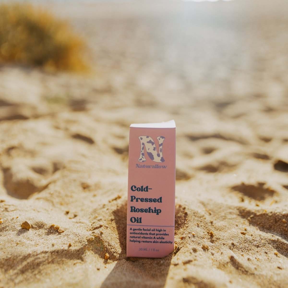 Naturallow's Organic Cold-Pressed Rosehip Oil box sitting in the sand