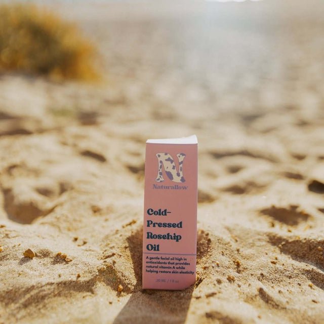 Naturallow's Organic Cold-Pressed Rosehip Oil box sitting in the sand