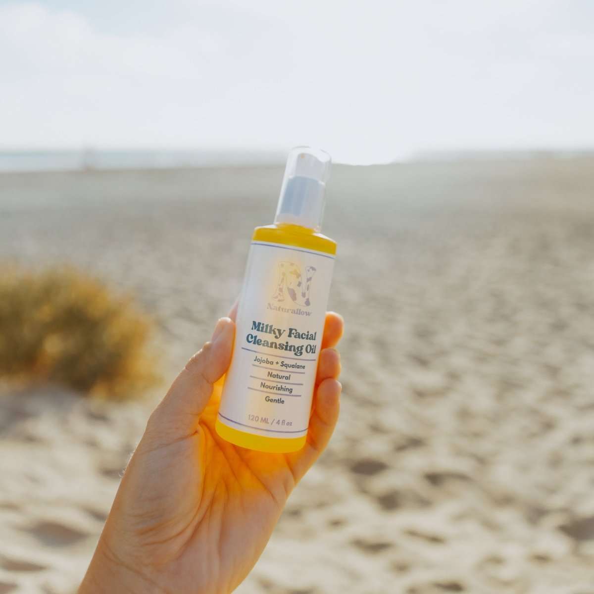 Naturallow's Milky Facial Cleansing Oil bottle being held up against the horizon