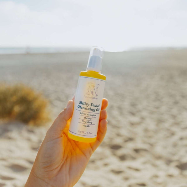 Naturallow's Milky Facial Cleansing Oil bottle being held up against the horizon