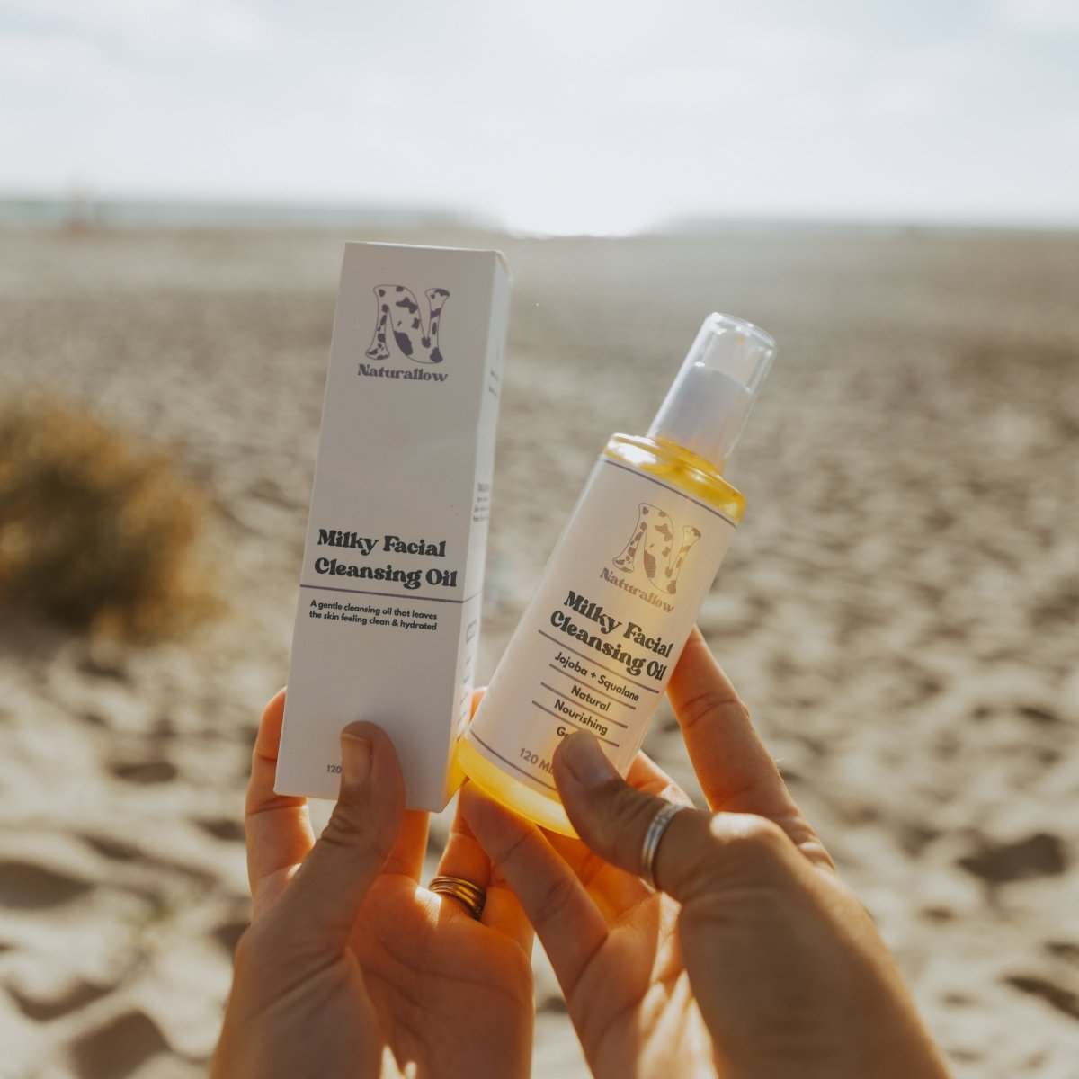 Naturallow's Milky Facial Cleansing Oil and it's box being held up next to each other against the horizon