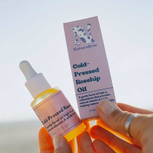 Naturallow's Organic Cold-Pressed Rosehip Oil and its box being held up against the horizon
