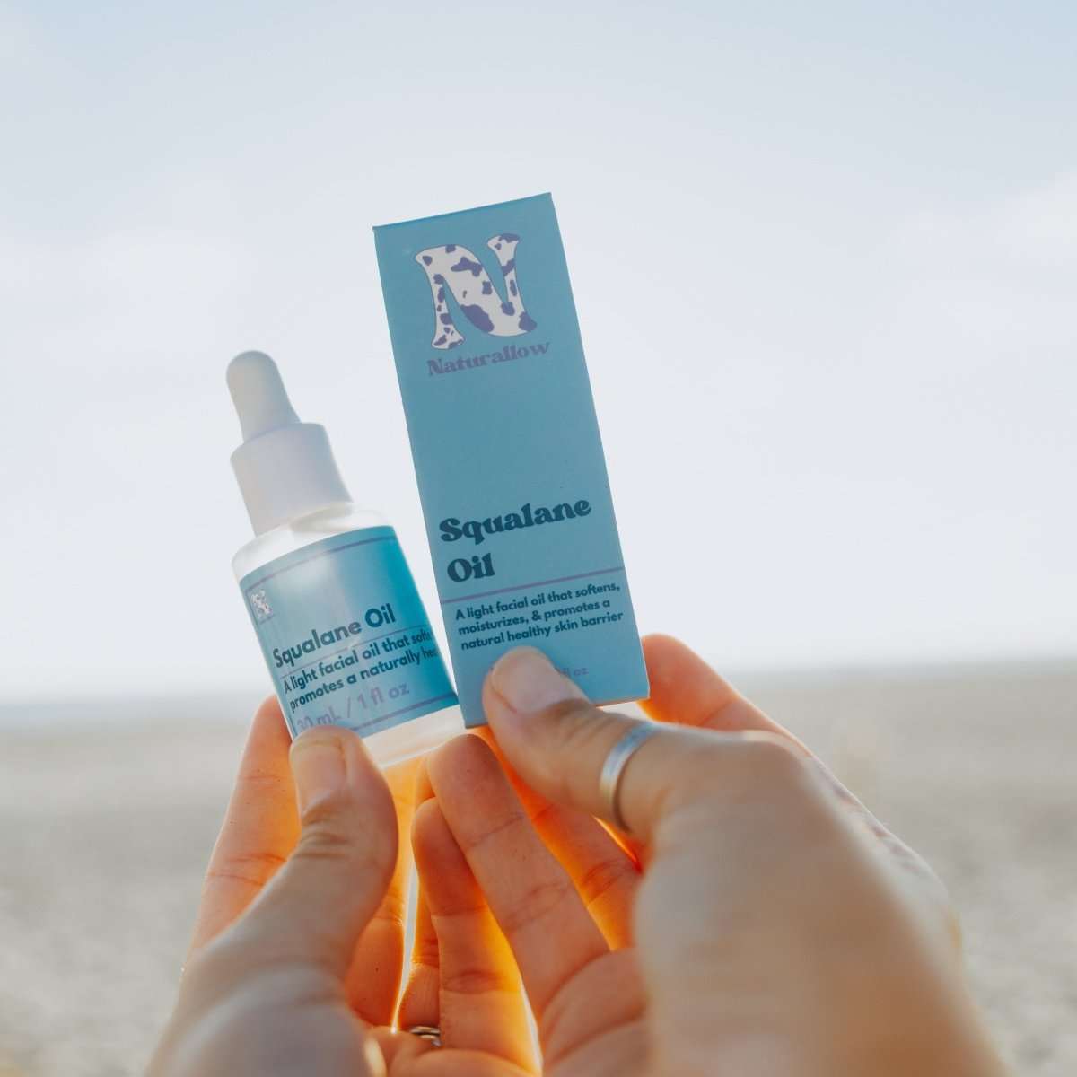 Naturallow's Organic Squalane Oil and its Box being held up against the horizon