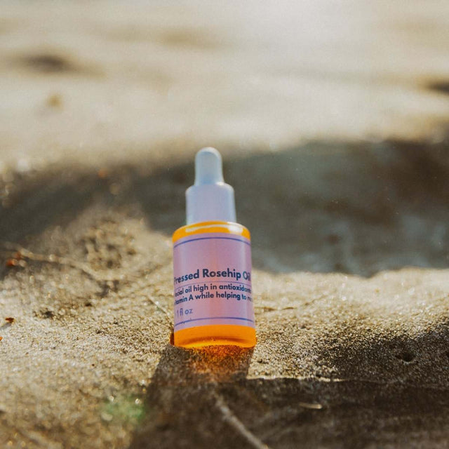 Naturallow's Organic Cold-Pressed Rosehip Oil bottle sitting in the sand