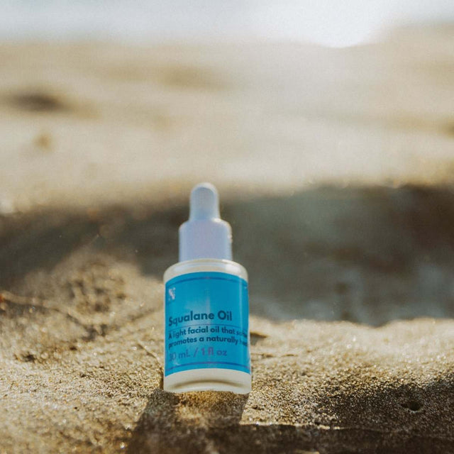 Naturallow's Organic Squalane Oil bottle sitting in the sand with the horizon in the background