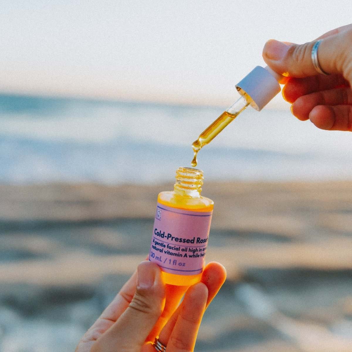 Naturallow's Organic Cold-Pressed Rosehip Oil with its dropper lid off being held up against the horizon
