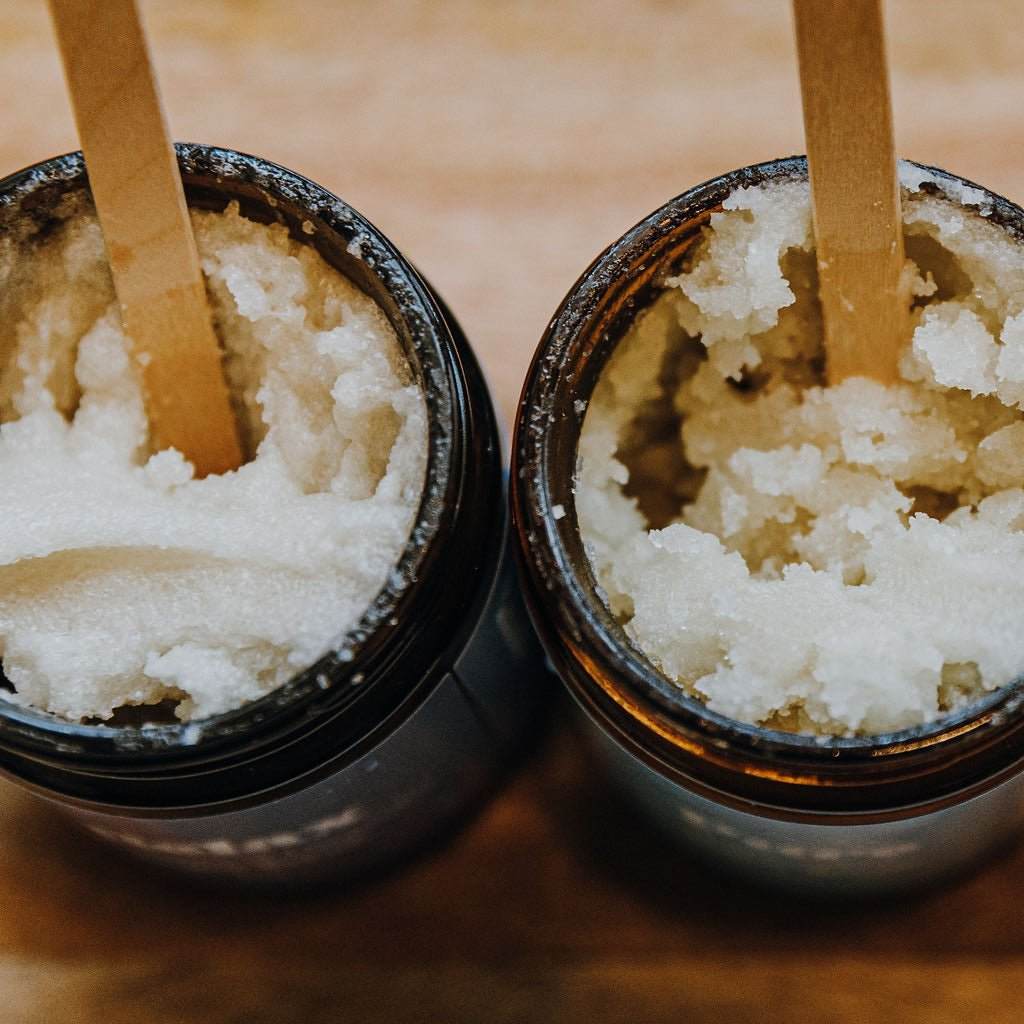 A top-down view of Naturallow's Sugar Scrub Jars lines up next to each other with stir sticks in them