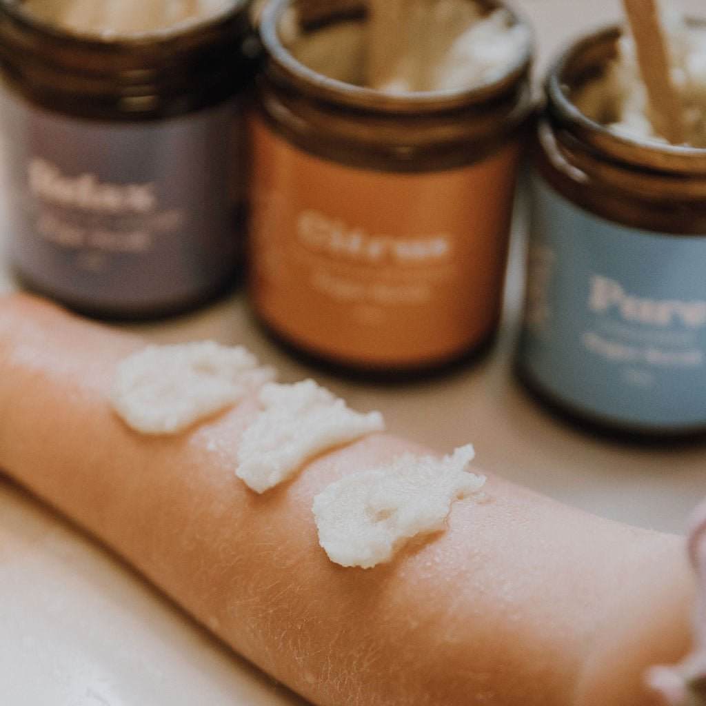 Naturallow's Sugar Scrub Jars lines up next to each other with small of the contents on an arm