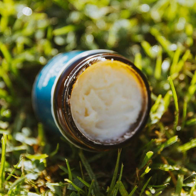 Naturallow's Tallow Magnesium Balm Jar leaned over without a lid in the grass showing the contents inside