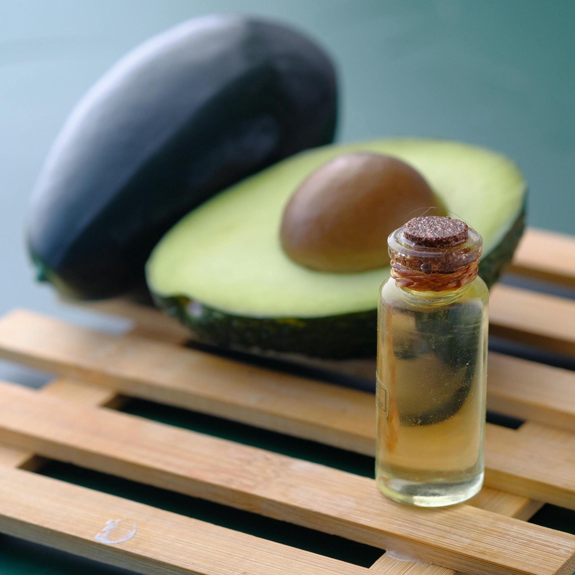 Bottle of avocado oil on a wooden surface with an avocado in the background