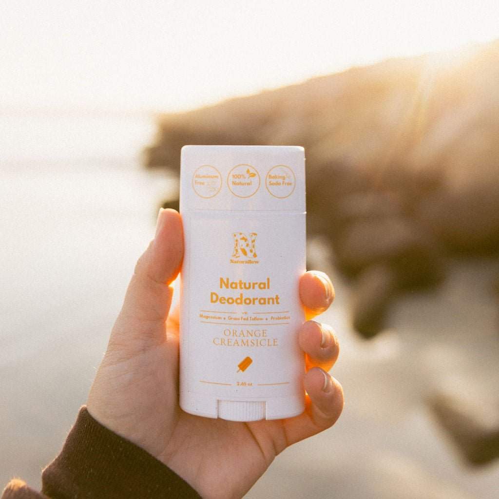 A hand holding up Naturallow's Limited Edition Orange Creamsicle Natural Deodorant against the horizon