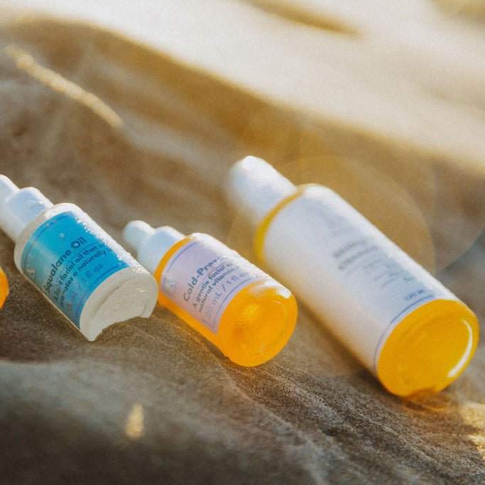 Naturallow 3-Step Hydration Bundle Product Image showing bottles of facial oils lying on the sandy beach